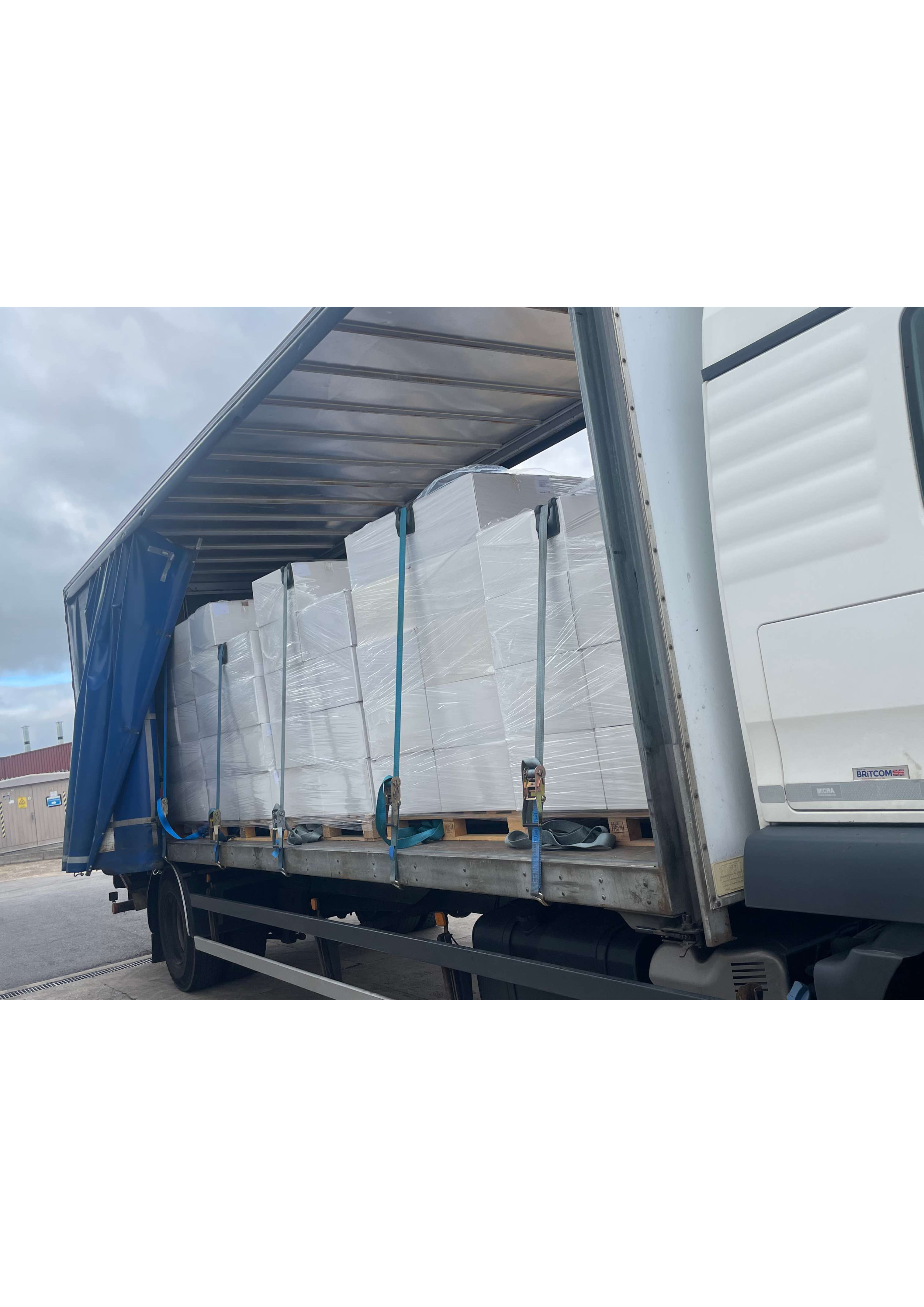 Trailer with curtain side fully open showing strapped shrink wrapped pallets on wooden pallets against a corrugated industrial building during a regional retail goods delivery