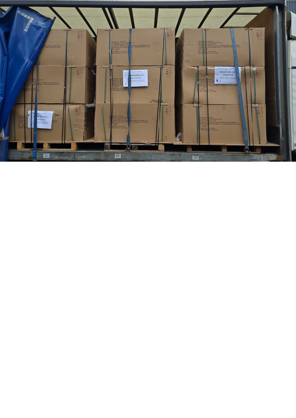 Multiple pallets of flat packed wardrobe boxes strapped with blue and black webbing inside a curtain sided lorry during a fragile regional freight delivery