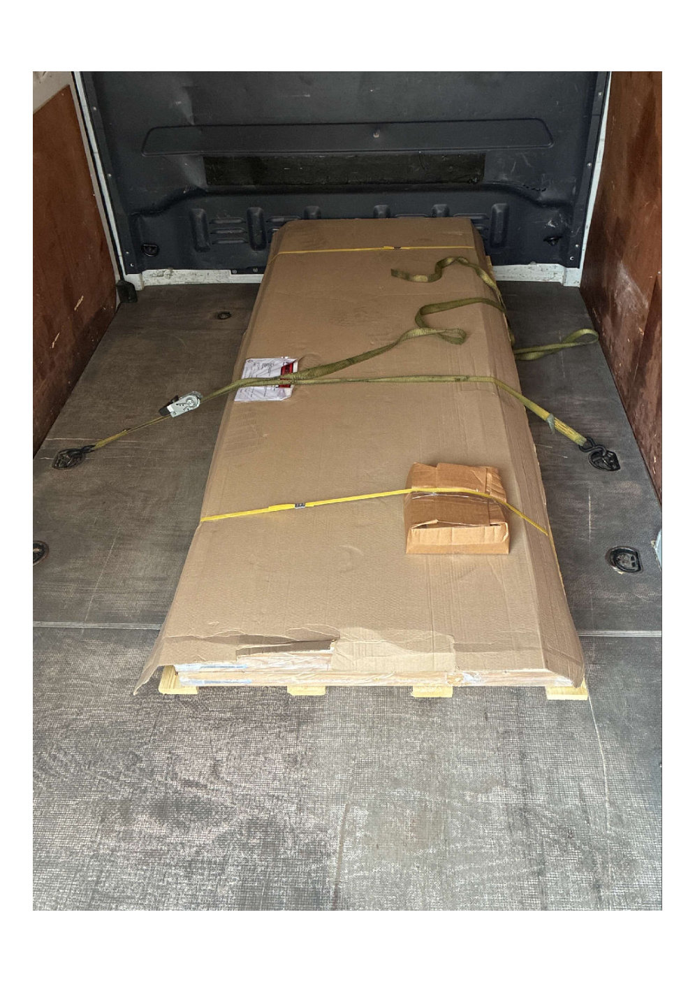 large oversized flat packed item secured with green and yellow straps on wooden pallets inside a delivery van