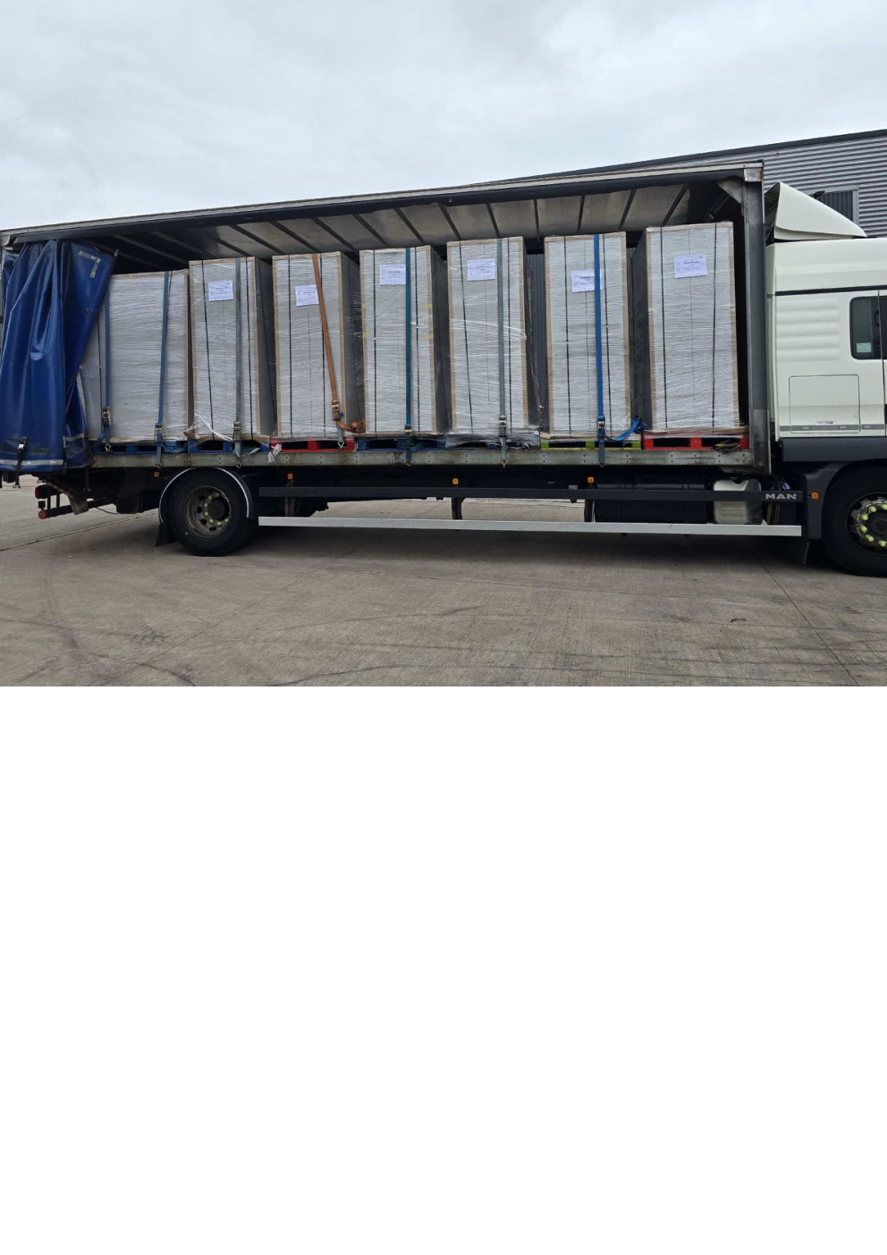White and blue curtain sided artic loaded with multiple tall shrink wrapped strapped pallets, parked on concrete surface during Midlands freight run