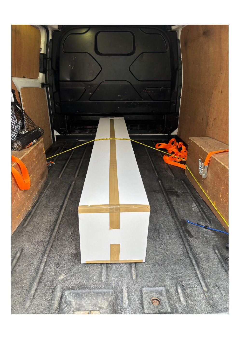 a single long packaged item secured inside a van load space with wooden panels ready for delivery